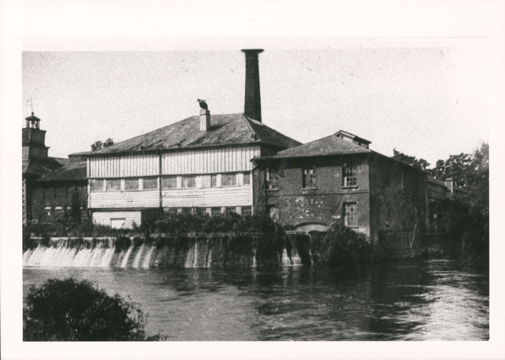 Black and white photograph of a paper mill from the outside surrounded by water.
