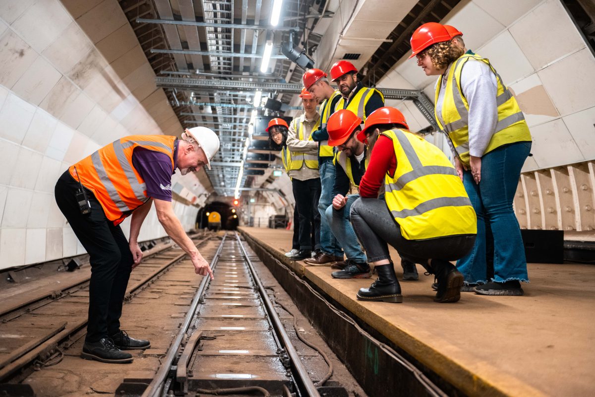 Tour guide Warwick points to the Mail Rail sleepers on a Tunnel Walk. The tour visitors crouch down to get a good view.